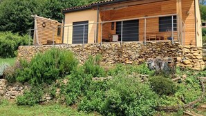 A wooden cabin with a stone foundation, large windows, and a covered porch area. - Gîte des Petites Pyrénées (AUSSEING)