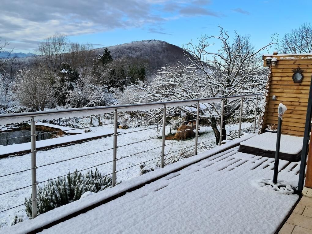 A snow-covered outdoor area with a wooden building, a metal railing, and a view of a mountain.