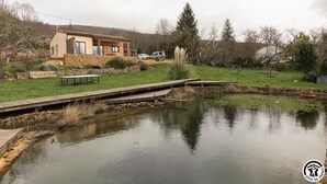 A house with a wooden deck, a pond, and a bench. - Gîte des Petites Pyrénées (AUSSEING)