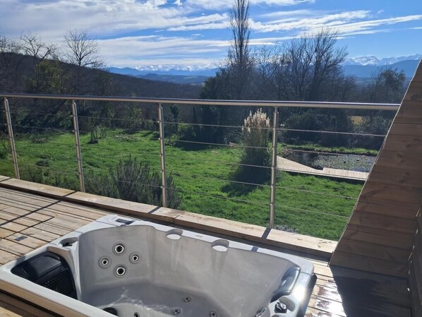 Ein Whirlpool auf einer Holzterrasse mit Blick auf eine grüne Landschaft und Berge im Hintergrund.