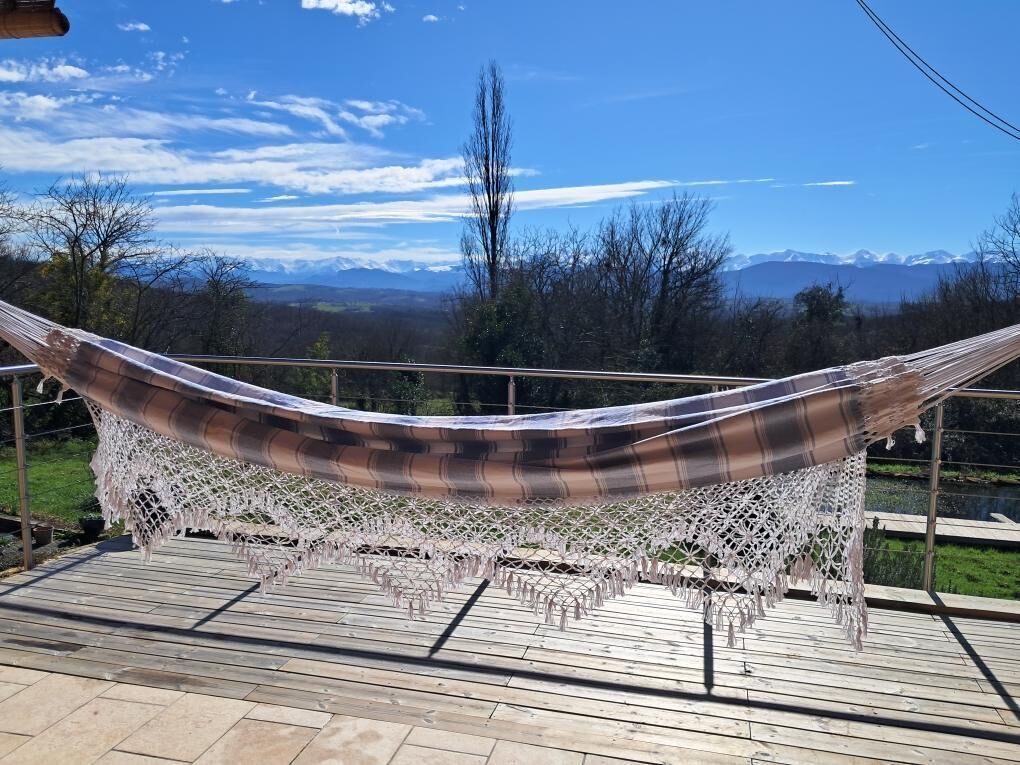 Un hamac sur une terrasse en bois, avec vue sur les montagnes et les arbres.