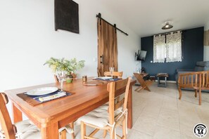 Ein Essbereich mit einem Holztisch, gedeckt für vier Personen, umgeben von Stühlen, einem Blumentopf und einem Weinglas.