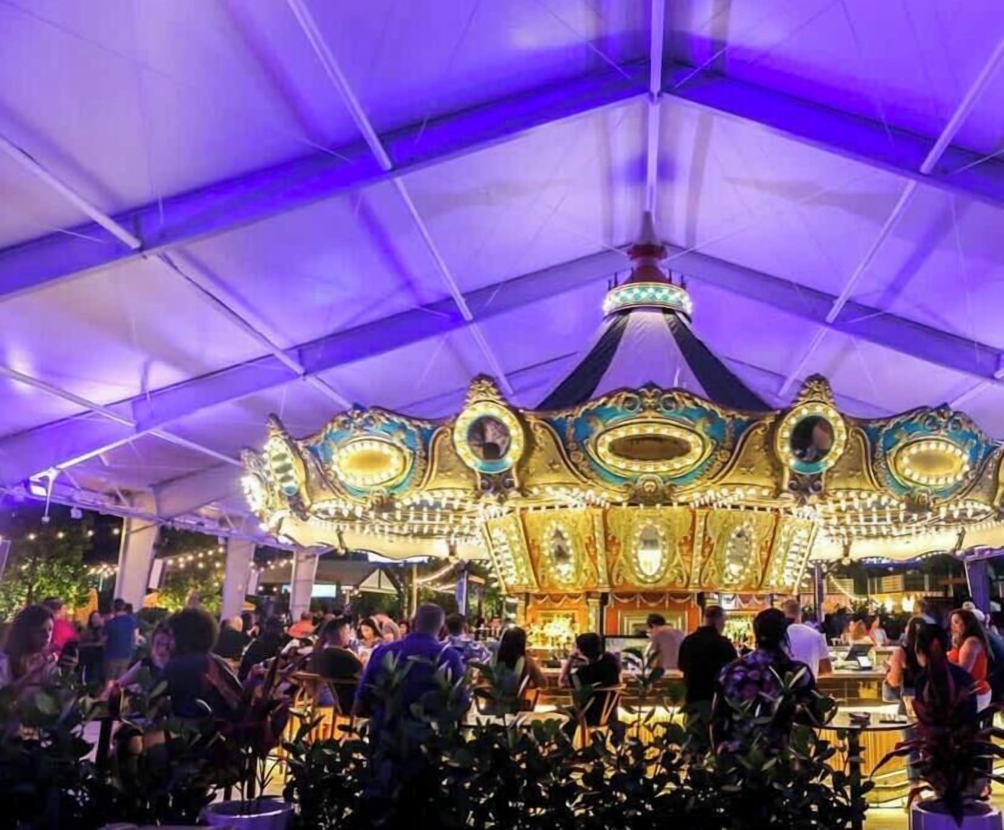 A carousel under a tent with a crowd of people.