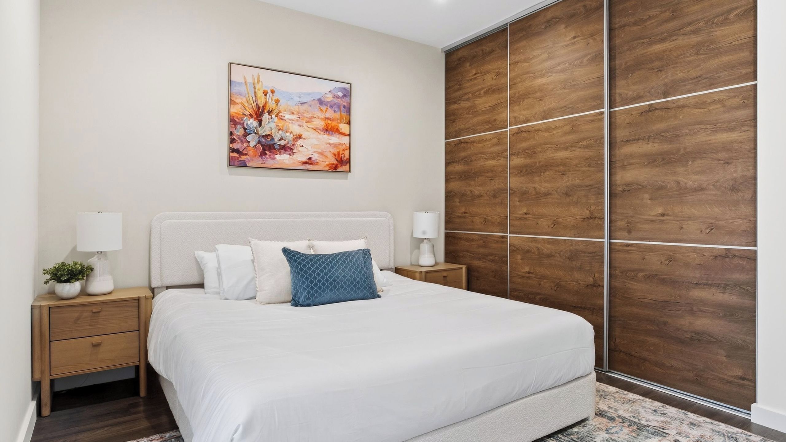Une chambre à coucher comprenant un lit, deux tables de chevet, une commode, une armoire en bois et un tableau accroché au mur.