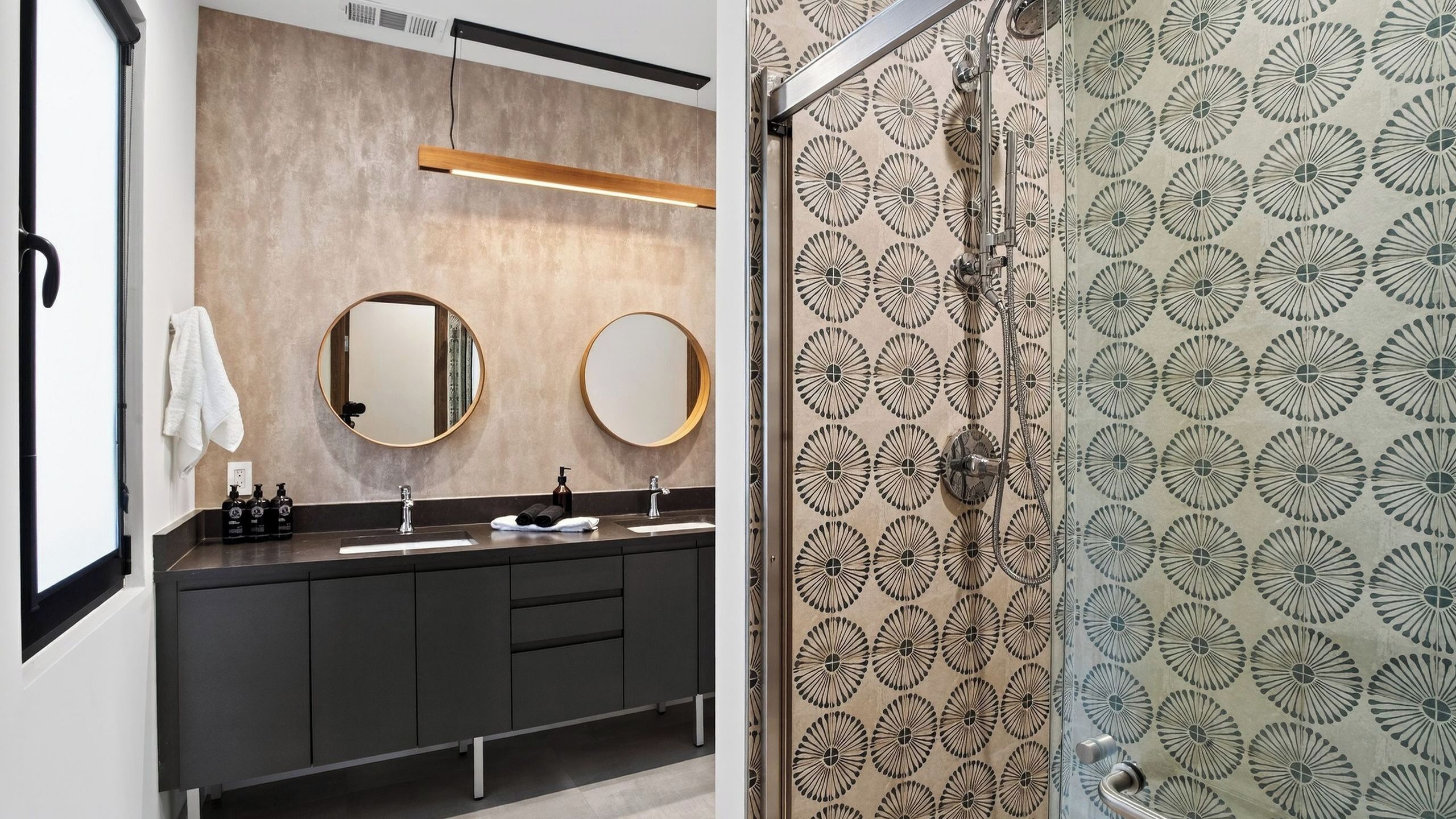 A modern bathroom with two sinks, a mirror, and a shower with a patterned wall.
