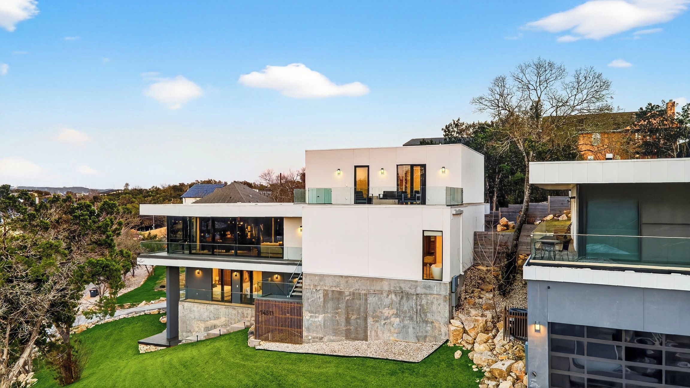 A modern two-story house with large glass windows, a stone facade, and a well-maintained lawn.