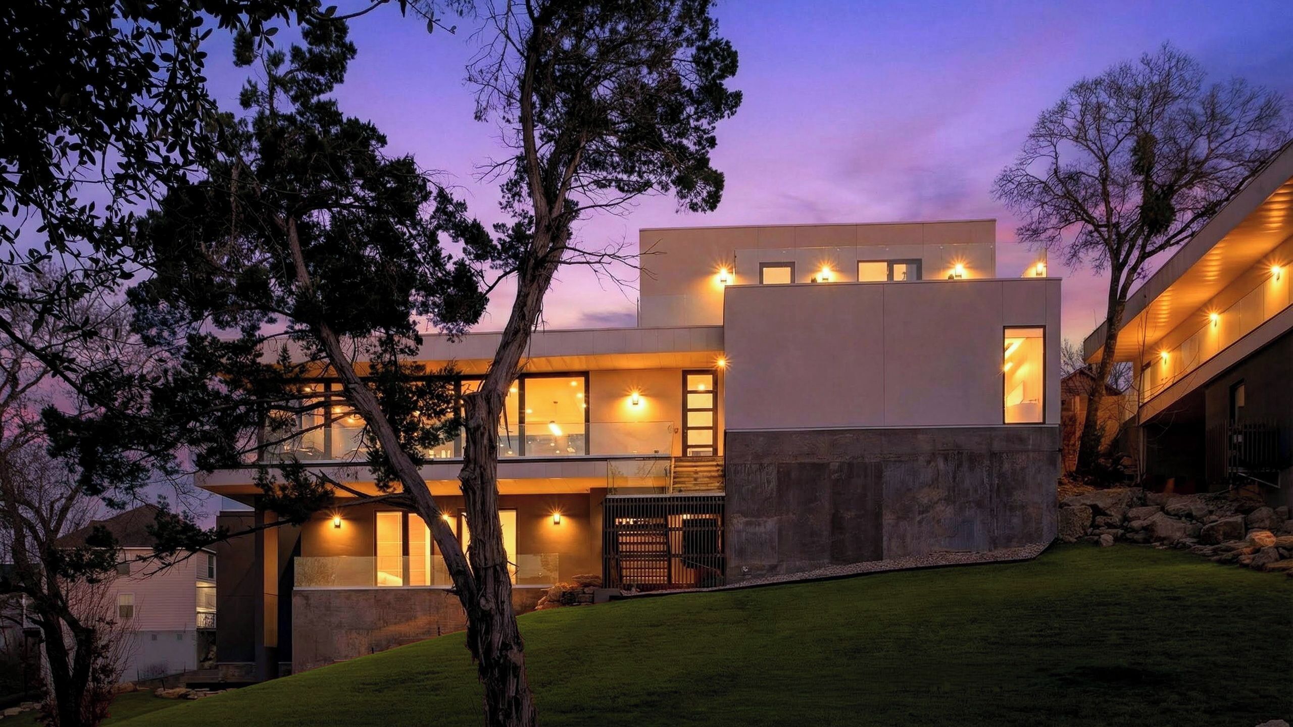 A modern two-story house with large windows and a well-lit exterior at dusk.
