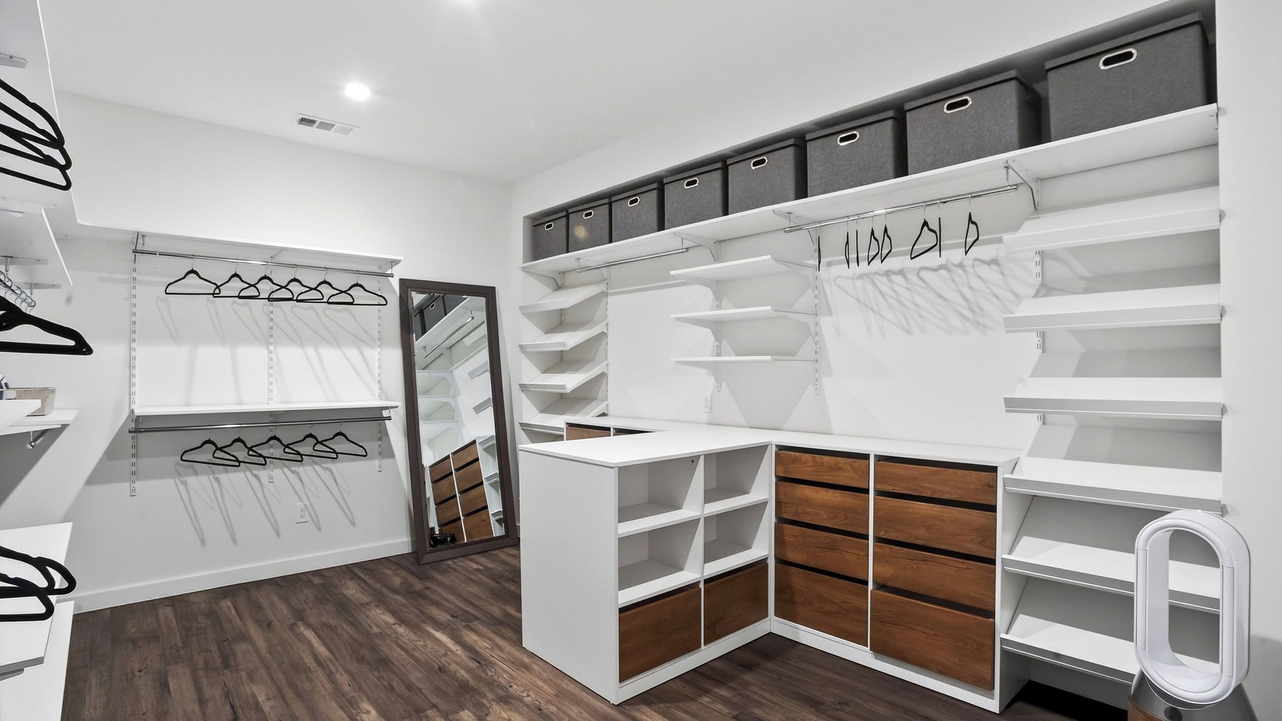A modern closet with white shelves, wooden drawers, and hanging space.