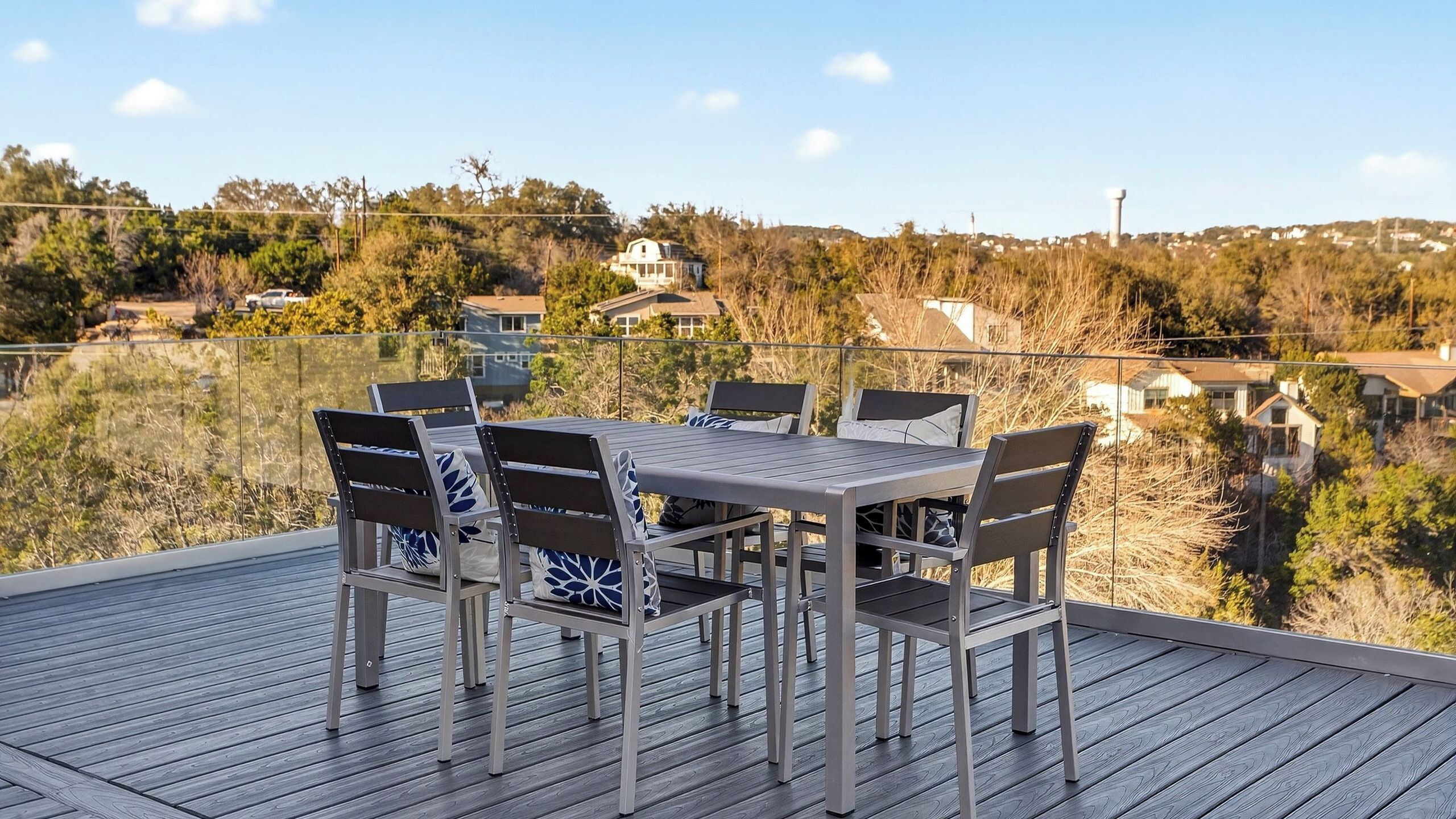 A deck with a table and chairs, overlooking a residential area with houses and trees.