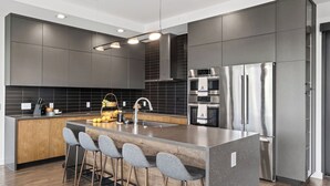 A modern kitchen with a central island, stainless steel appliances, and a dark backsplash. - Hunters Estate by Avantstay Design-forward Hillside Home Private Pool + Firepit Close to Lake Travis + Downtown Austin (Austin)