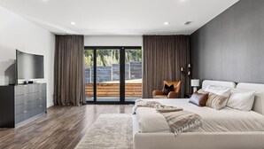 A modern bedroom with a large bed, a TV, and a sliding glass door leading to a balcony. - Hunters Estate by Avantstay Design-forward Hillside Home Private Pool + Firepit Close to Lake Travis + Downtown Austin (Austin)