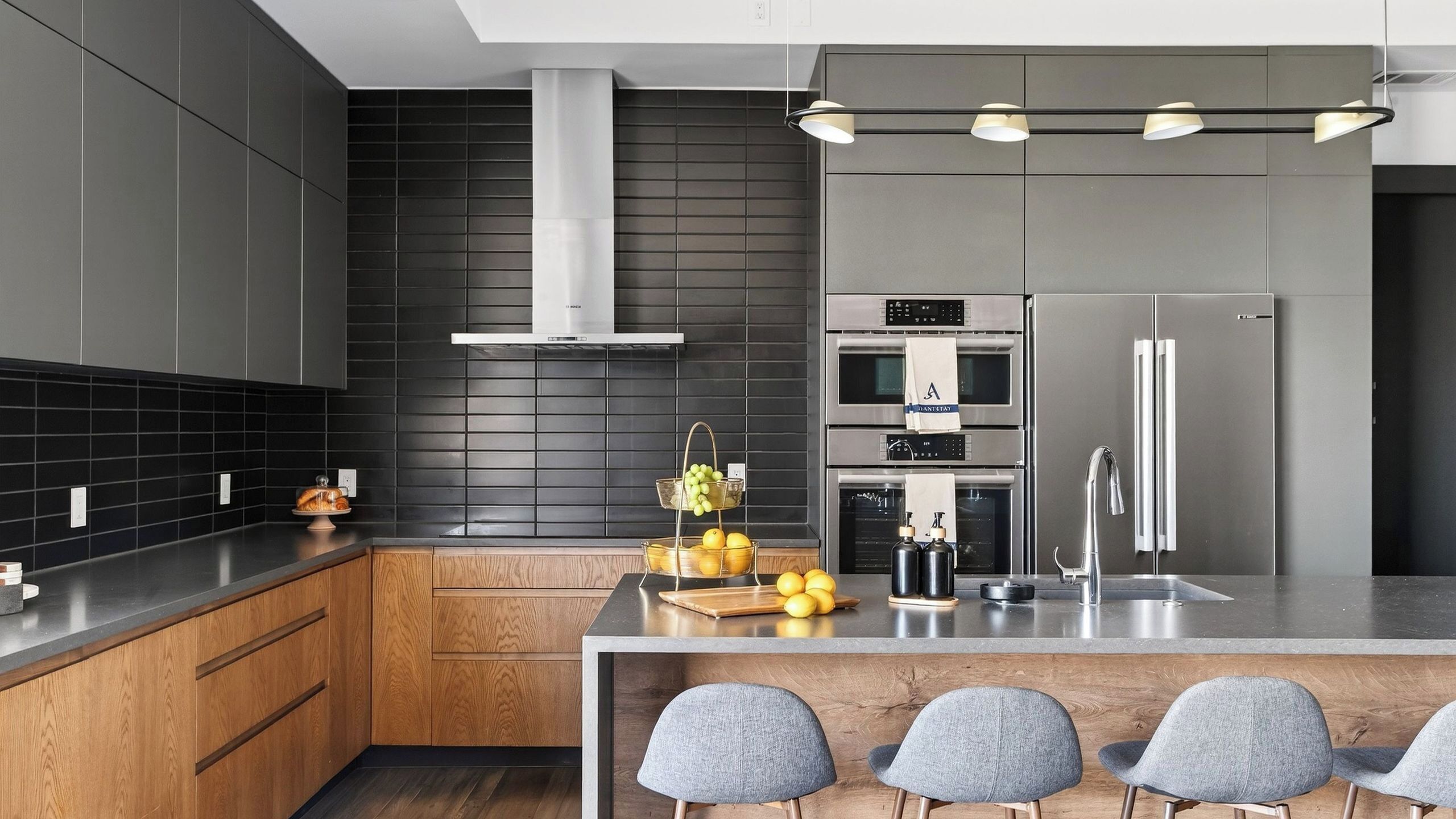 A modern kitchen with dark cabinetry, a central island with seating, stainless steel appliances, and a black tiled backsplash.