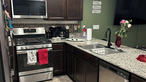 A modern kitchen with dark wooden cabinets, stainless steel appliances, a granite countertop, and a tiled floor. - Bri’s Place Cozy 2BR Home Near Nellis AFB & Speedway (Las Vegas)