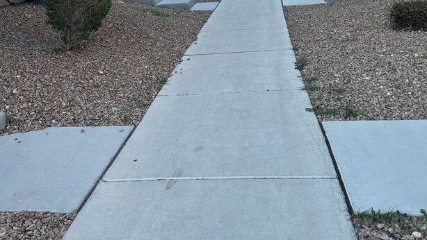 A pathway leading through a row of uniform buildings with a consistent architectural style, featuring a central walkway flanked by small bushes and pebbles. - Bri’s Place Cozy 2BR Home Near Nellis AFB & Speedway (Las Vegas)