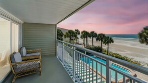 A balcony with a wicker chair, a pool, and a view of the beach. - Beachfront Bliss - Outdoor Pool - Sleeps 6 (Belleair Beach)