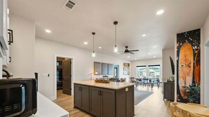 Eine moderne Küche mit Kochinsel, Holzboden, Pendelleuchten und Deckenventilator.