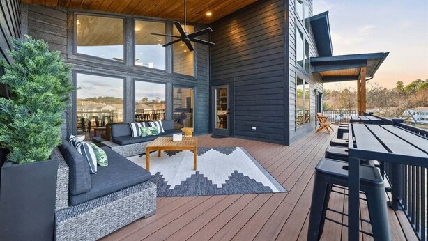 Ein modernes Haus mit Terrasse, Sitzgelegenheiten im Freien und großen Fenstern.