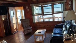 L’intérieur d’un chalet en bois, avec un canapé, une table, une chaise et une vue sur un lac, visible à travers de grandes fenêtres.