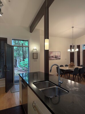 A modern kitchen with a black countertop, stainless steel sink, and a dining area with a table and chairs.