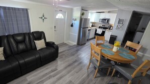 A living room with a black leather sofa, a dining table with chairs, a kitchen area with white cabinets, a refrigerator, and a microwave. - Lovely 3-bedroom mobile home with AC in charming Largo (Largo)