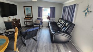 A living room with a TV, a painting, a sofa, a chair, a small table, and a fan. - Lovely 3-bedroom mobile home with AC in charming Largo (Largo)