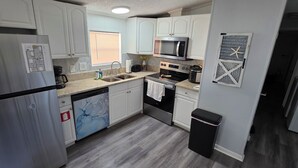 A compact kitchen with white cabinets, a stainless steel refrigerator, a microwave, an oven, and a dishwasher. - Lovely 3-bedroom mobile home with AC in charming Largo (Largo)
