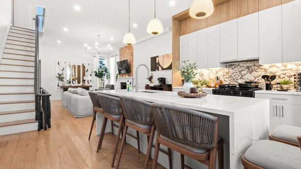 A modern kitchen with a central island, bar stools, pendant lighting, and a staircase. - The Bergen Standard  3BD 2BA Brownstone + Parking (Jersey City)