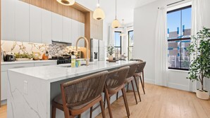A modern kitchen with a marble island, wooden cabinets, pendant lighting, and a large window with a view. - The Bergen Standard  3BD 2BA Brownstone + Parking (Jersey City)