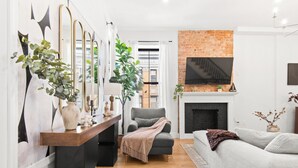 A living room with a fireplace, a sofa, a chair, and a TV mounted on the wall. - The Bergen Standard  3BD 2BA Brownstone + Parking (Jersey City)