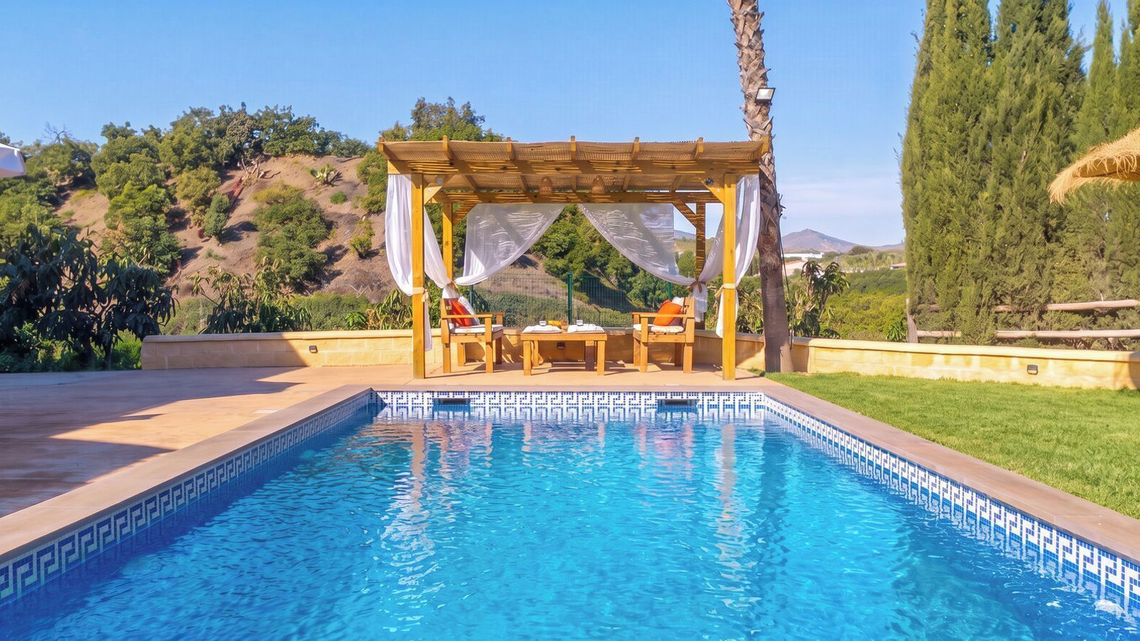 Une piscine agrémentée d’une pergola et d’un espace détente, le tout entouré de verdure et de collines.