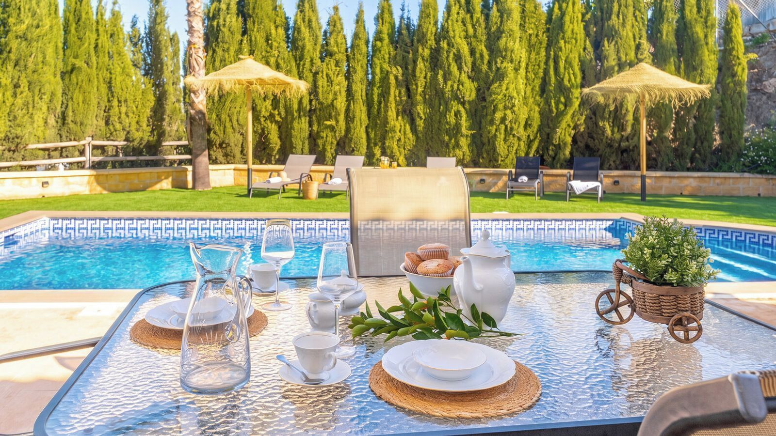 Desayuno junto a la piscina con mesa, sillas y vista al agua y a los árboles.