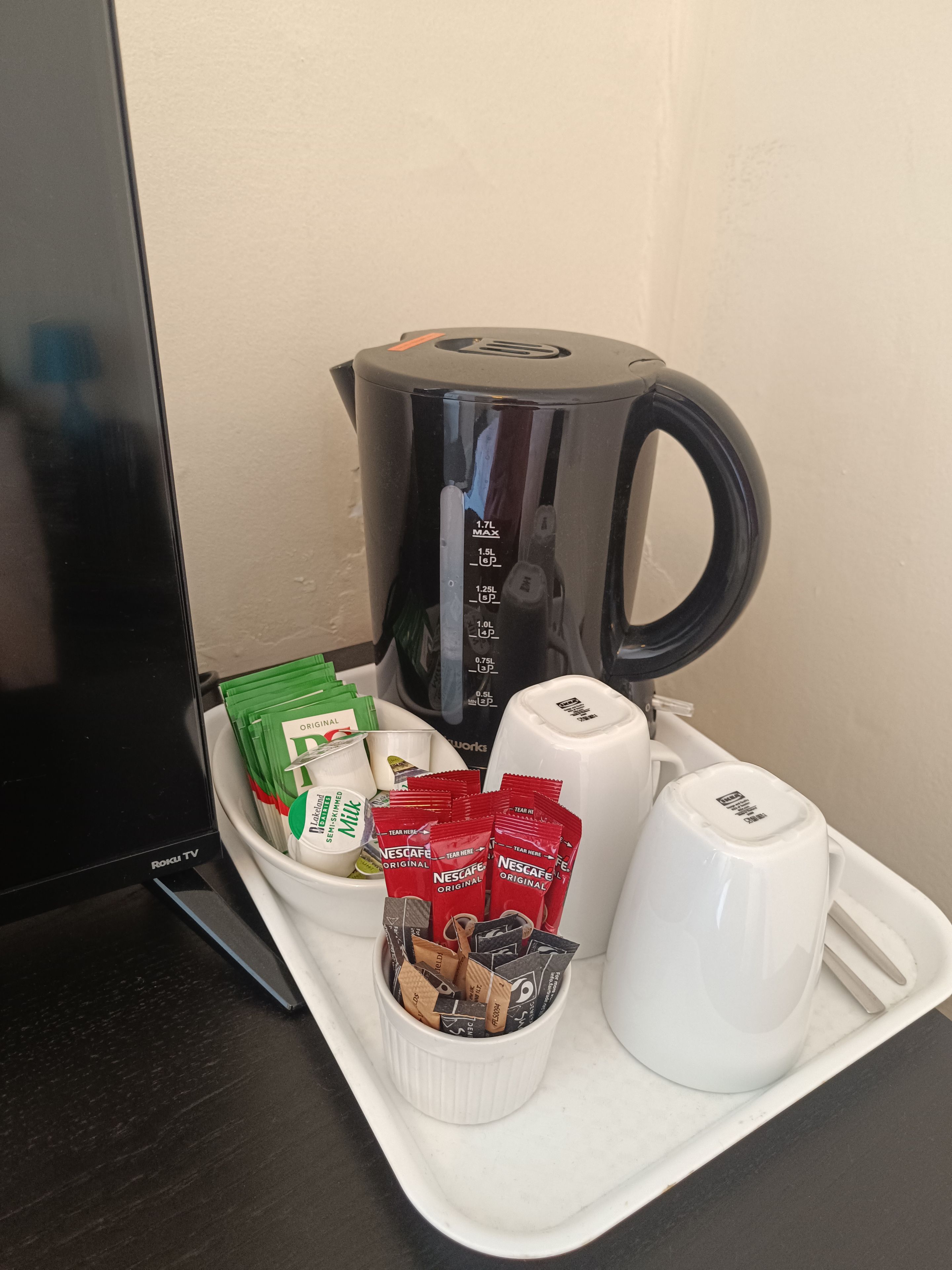 A tray with a coffee maker, a TV, and various beverage packets.