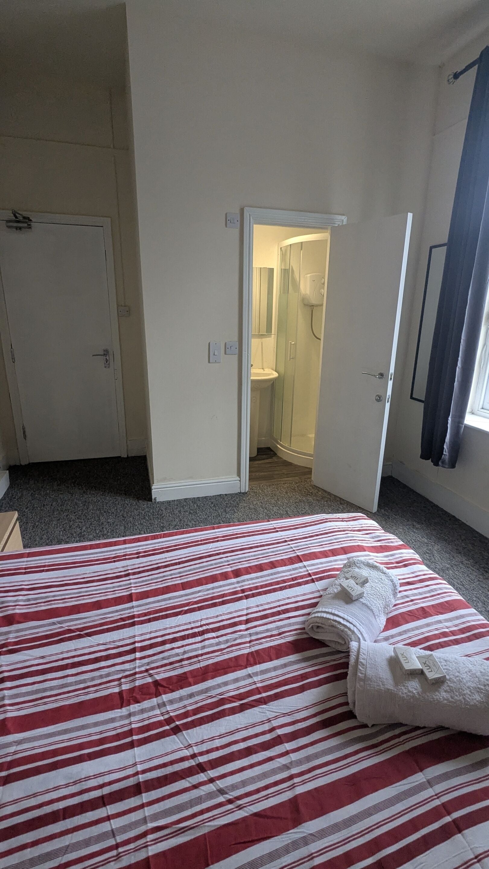 A hotel room with a bed, a bathroom with a shower, and a door leading to another room.