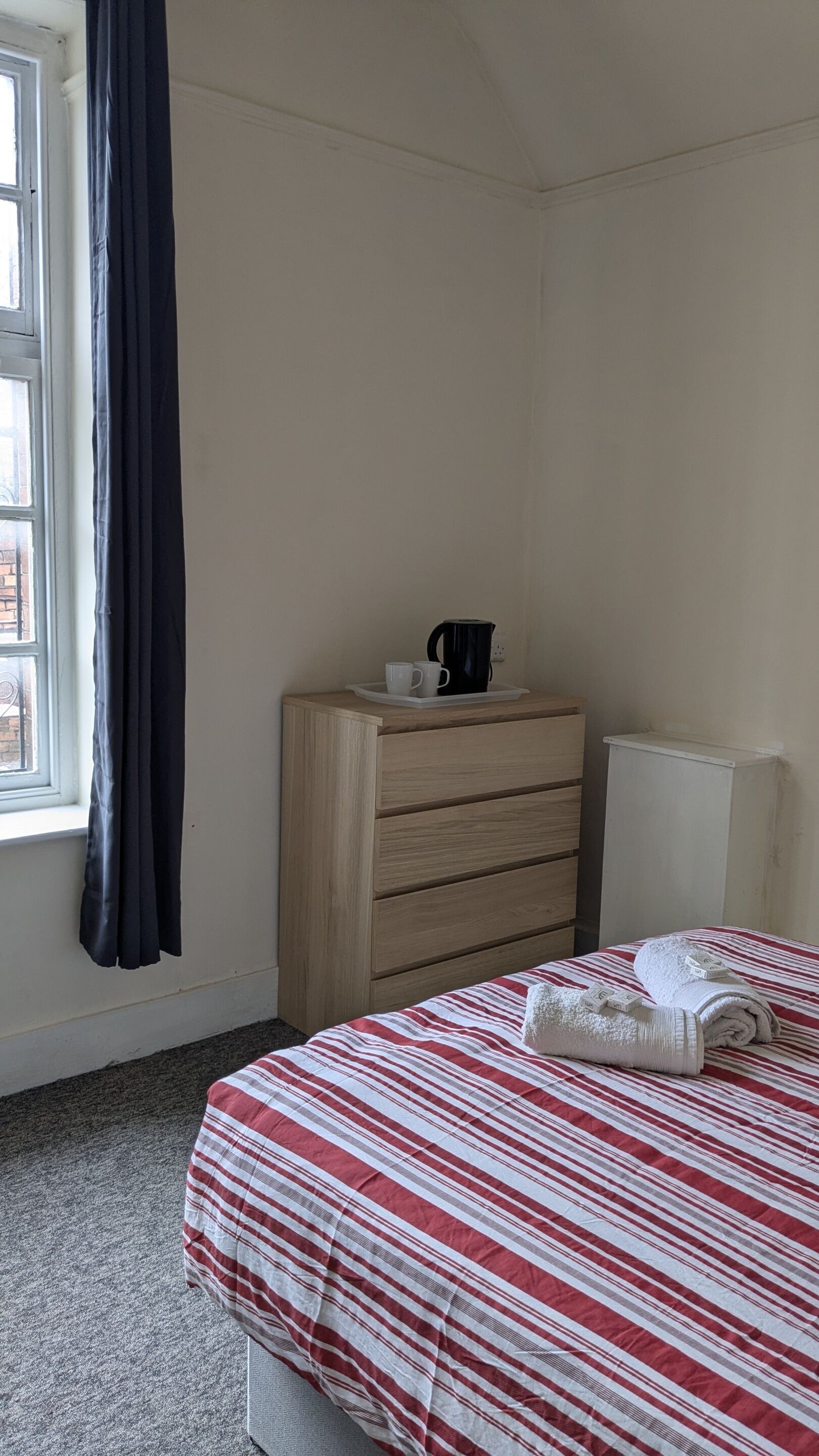Un dormitorio con una cama, un aparador, un radiador y una ventana con cortinas.