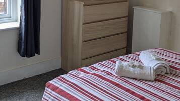Un dormitorio con una cama, un aparador, un radiador y una ventana con cortinas.