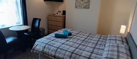 Habitación de hotel con cama, escritorio, silla, cómoda, televisor y ventana.