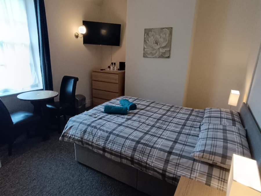 Een hotelkamer met een bed, een bureau, een stoel, een dressoir, een televisie en een raam.