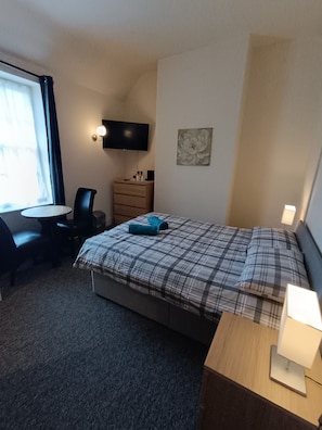 Een hotelkamer met een bed, een bureau, een stoel, een dressoir, een televisie en een raam.