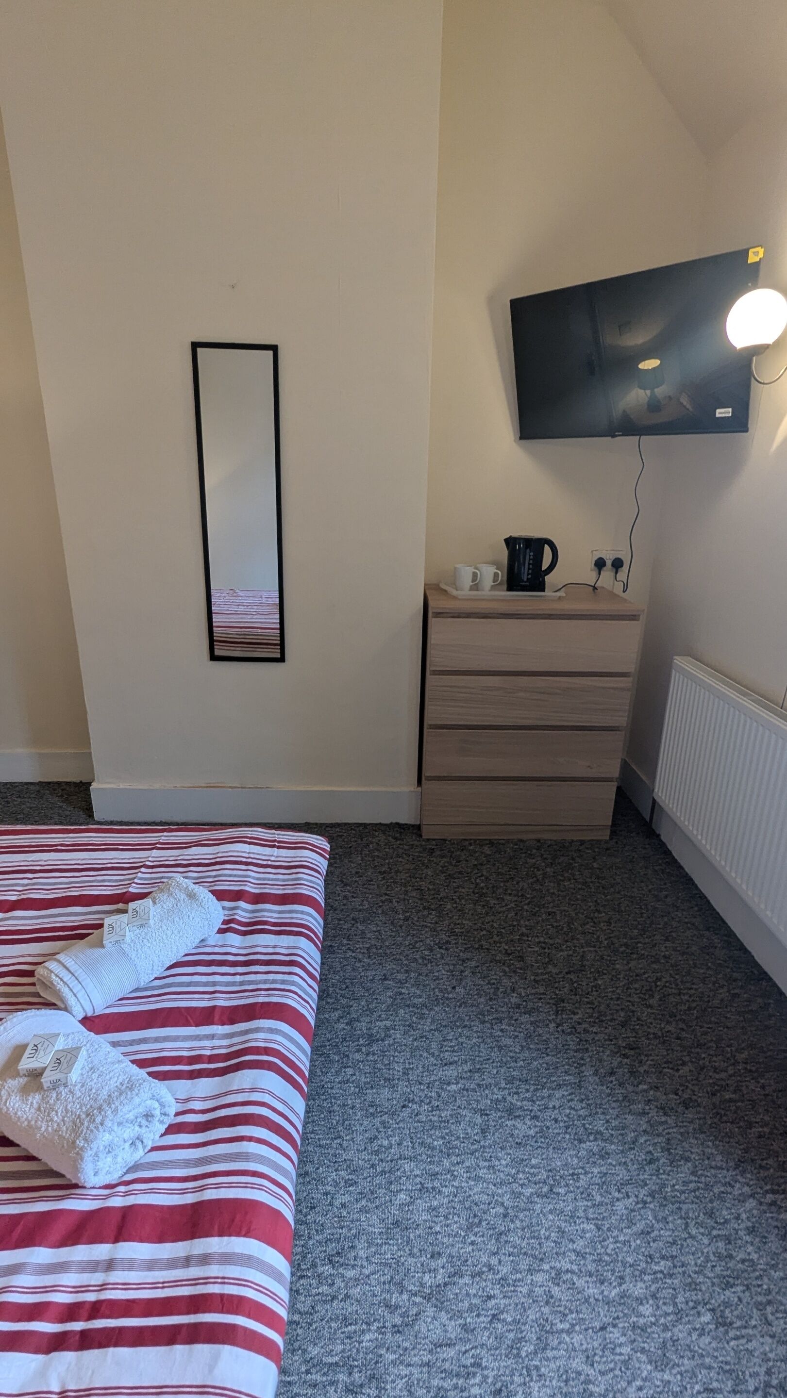 Una habitación de hotel con cama, cómoda, televisor de pantalla plana montado en la pared y radiador.