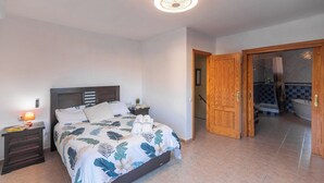A bedroom with a bed, nightstand, and a bathroom visible through an open door. - Casa Luis Canillas de Aceituno by Ruralidays (Málaga)
