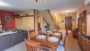 A dining area with a wooden table set for four, surrounded by wooden chairs. A stone wall and a staircase are visible in the background. - Casa Luis Canillas de Aceituno by Ruralidays (Málaga)