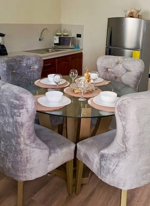 A dining area with a round glass table, four grey upholstered chairs, and a decorative centerpiece.