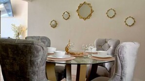 A dining area with a round glass table, grey upholstered chairs, white plates, and gold decorative mirrors on the wall. - ARENA DORADA (Puerto Baquerizo Moreno)