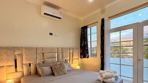 A modern bedroom with a large bed, bedside lamps, an air conditioning unit, and a view through a sliding glass door. - ARENA DORADA (Puerto Baquerizo Moreno)