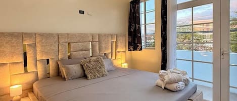 A modern bedroom with a large bed, bedside lamps, an air conditioning unit, and a view through a sliding glass door.