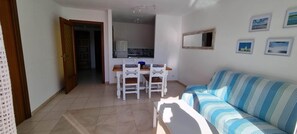 A living room with a striped sofa, a dining table with chairs, and a kitchen area in the background. - Centrally located apartment, 5 min from the beach. Perfect to enjoy with the family (Tossa de Mar)