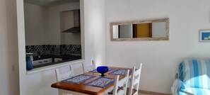 A dining area with a wooden table, blue placemats, and white chairs. A blue bowl is on the table. A kitchen with a black range hood is visible in the background. - Centrally located apartment, 5 min from the beach. Perfect to enjoy with the family (Tossa de Mar)