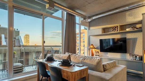 Ein modernes Wohnzimmer mit Essbereich, großen Fenstern, einem Flachbildfernseher und Blick auf die Stadt.