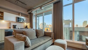 Ein modernes Wohnzimmer mit einer Couch, Hocker und einem großen Fenster mit Blick auf die Stadt.