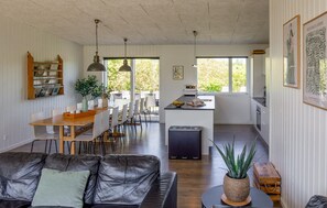 Una cocina moderna con una isla central, comedor con sillas, un sofá de cuero y una planta en maceta.